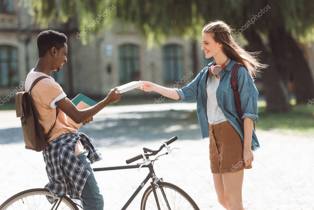 multiethnic couple with books and bicycle