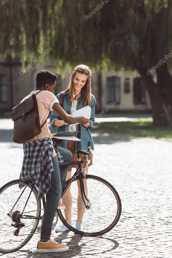 multiethnic couple with books and bicycle