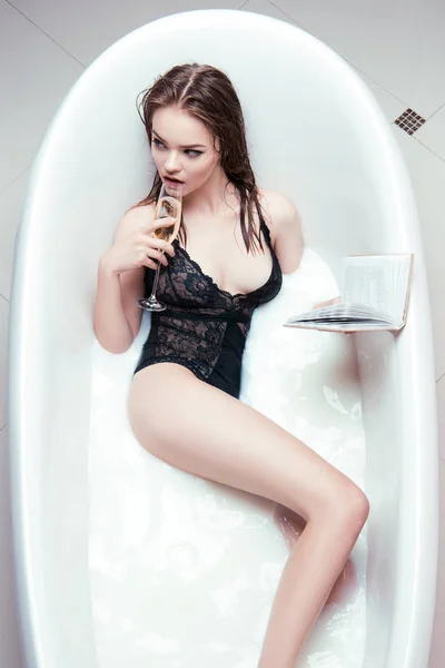 Женщина с бокалом шампанского и забронировать в ванной — стоковое фото