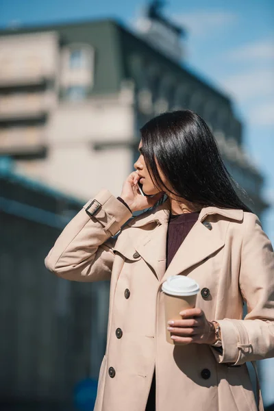 Woman in trench coat talking by phone — Free Stock Photo