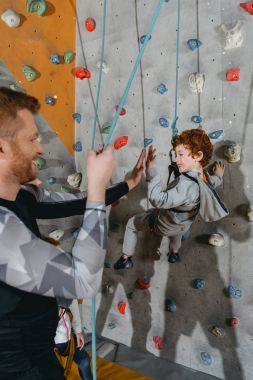 Boy on climbing wall high-fiving father clipart