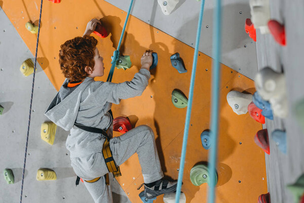 Little boy climbing wall with grips