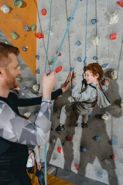 Boy on climbing wall high-fiving father