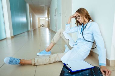 Tired doctor sitting in hospital corridor clipart