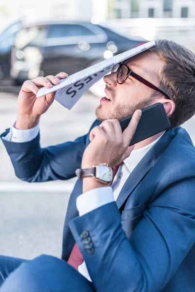 Stressed businessman with newspaper and smartphone — Stock Photo, Image