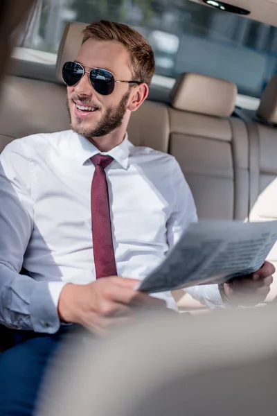 businessman with newspaper on backseat of car