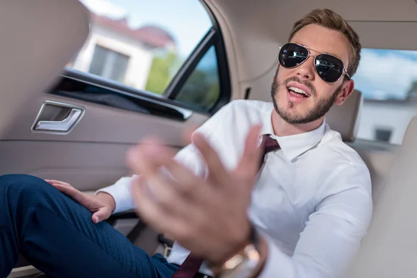 Homem de negócios em óculos de sol no banco de trás do carro — Fotografia de Stock