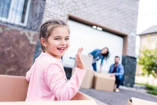 Mädchen sitzt in Kiste und winkt in Kamera — Stockfoto