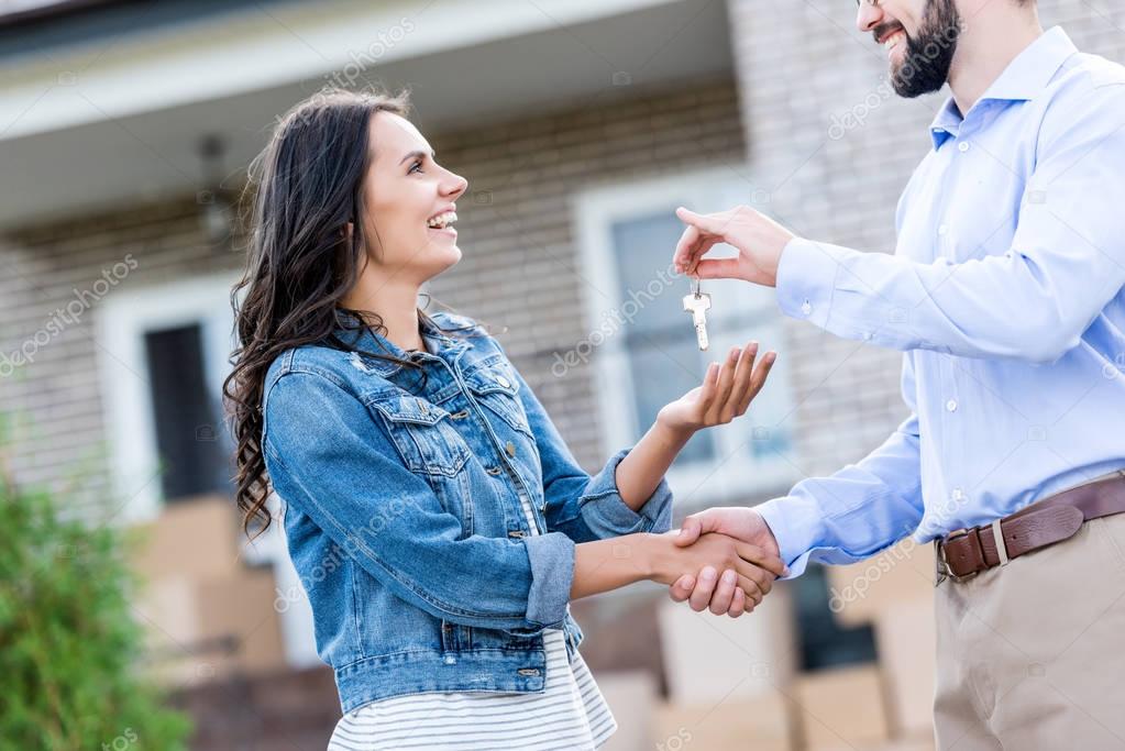 Young happy woman buying new house and taking keys from realtor