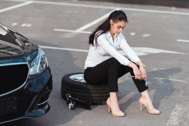 İngiliz anahtarı ile lastik üzerinde oturan kadın