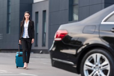 Woman walking with suitcase in parking lot clipart