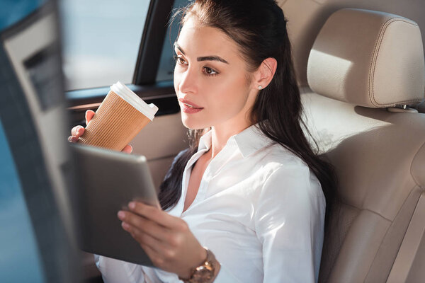 woman in car with digital tablet and coffee