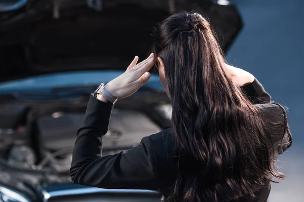 Проблемная женщина смотрит на двигатель автомобиля — стоковое фото