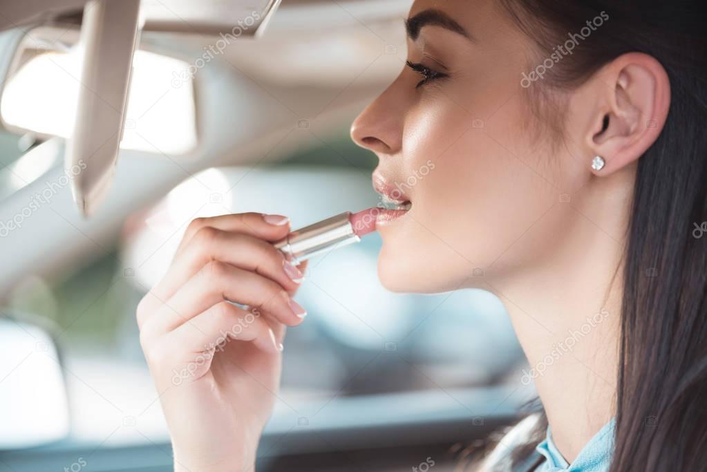 woman applying lipstick in car
