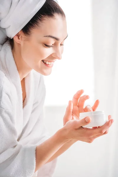 Mujer en albornoz aplicando crema facial — Foto de Stock