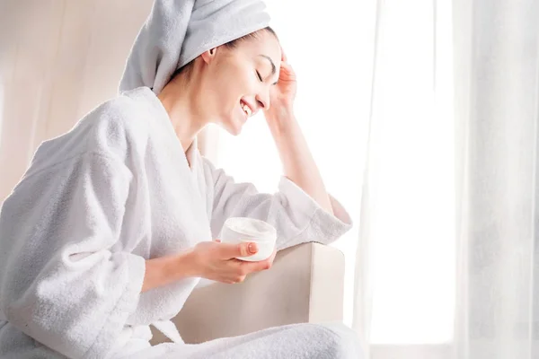 Woman in bathrobe holding jar of cream — Stock Photo, Image