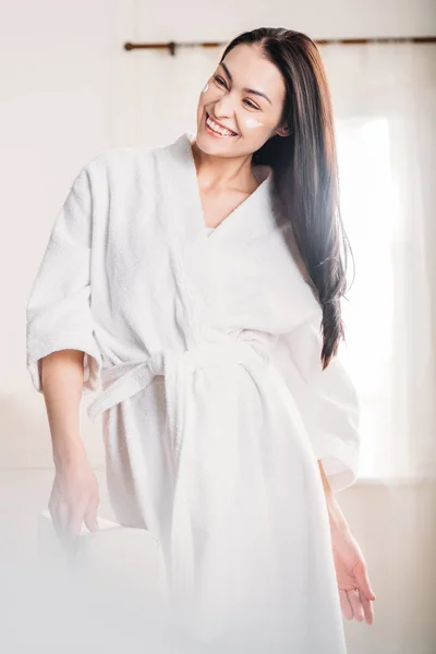 Young woman in bathrobe with cream on face — Stock Photo, Image