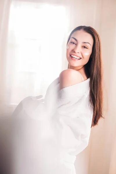 Young woman in bathrobe with cream on face — Stock Photo, Image