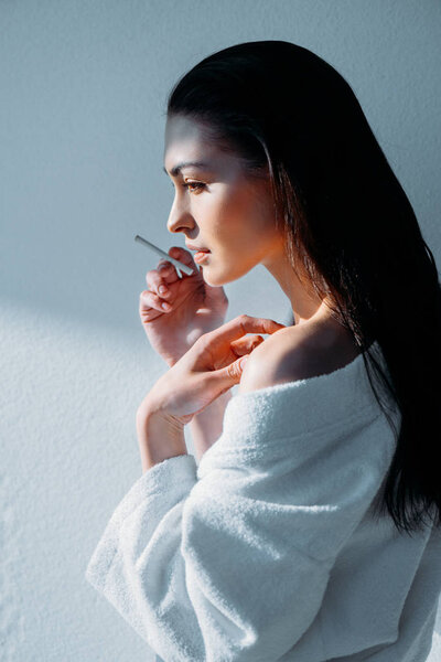Young woman in bathrobe smoking