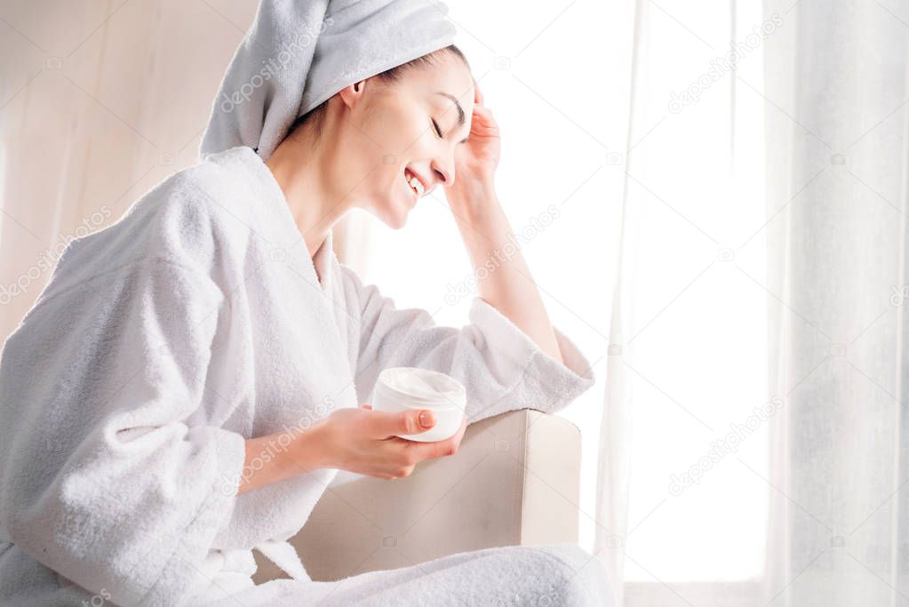 woman in bathrobe holding jar of cream