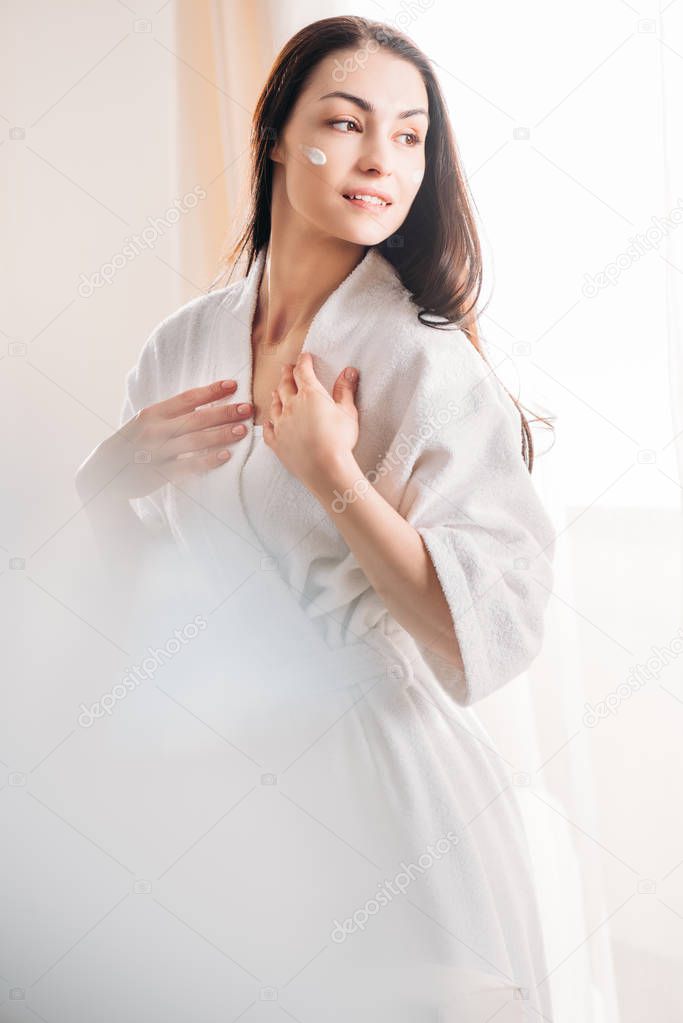 Relaxed woman in bathrobe with cream on face