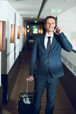businessman walking in hotel with smartphone clipart