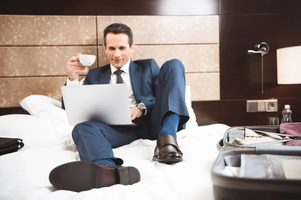 Улыбающийся бизнесмен на кровати с помощью ноутбука — стоковое фото