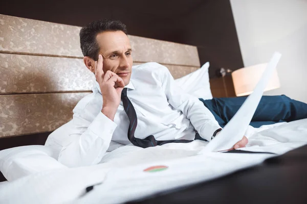 Businessman on bed reading paperwork — Free Stock Photo