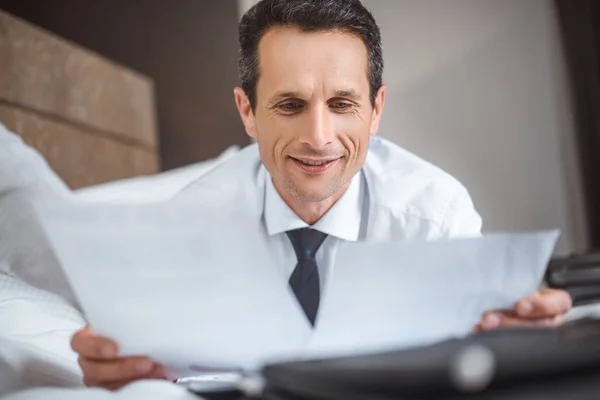 Zakenman op bed lezen papierwerk — Stockfoto