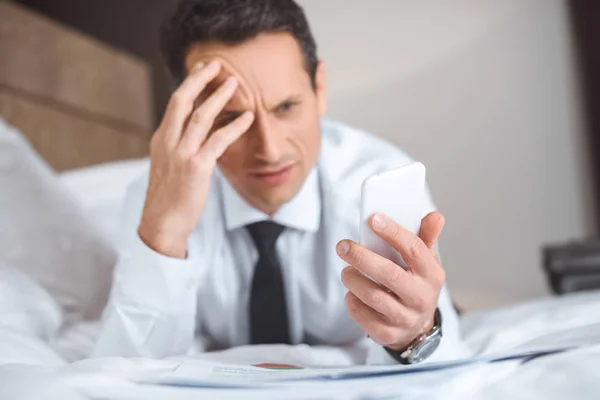 Businessman on bed using smartphone — Stock Photo, Image