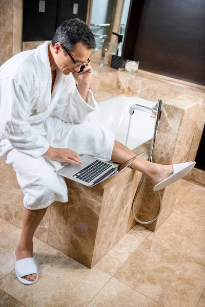 Empresário em roupão de banho trabalhando com dispositivos — Fotos gratuitas