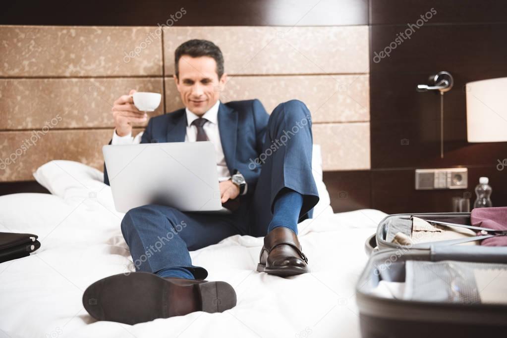 Smiling businessman on bed using laptop