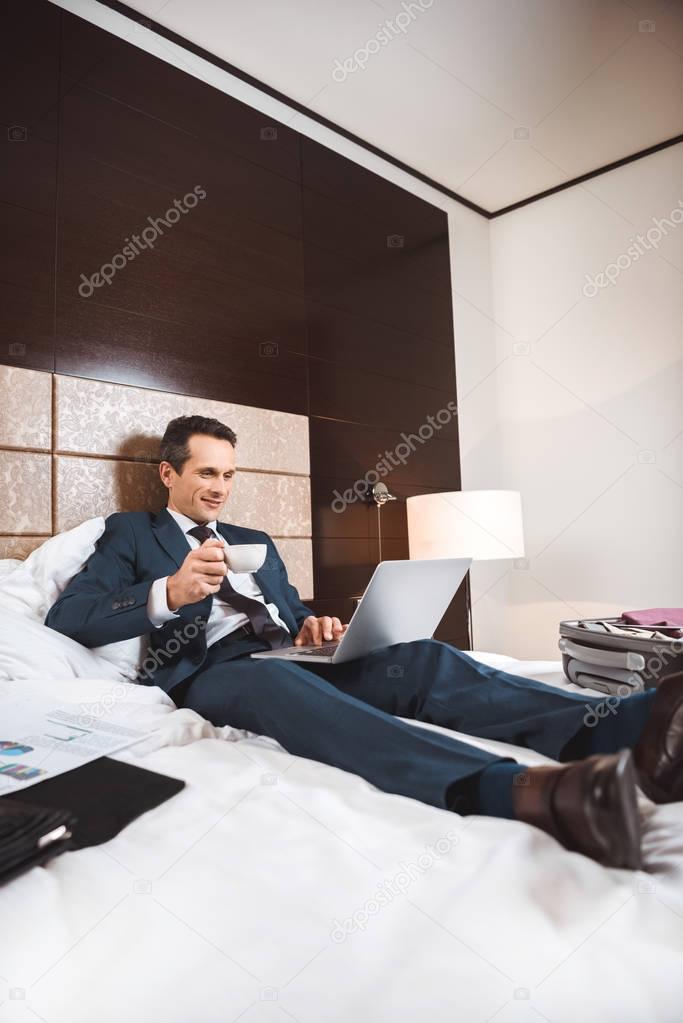 businessman on bed with laptop and coffee