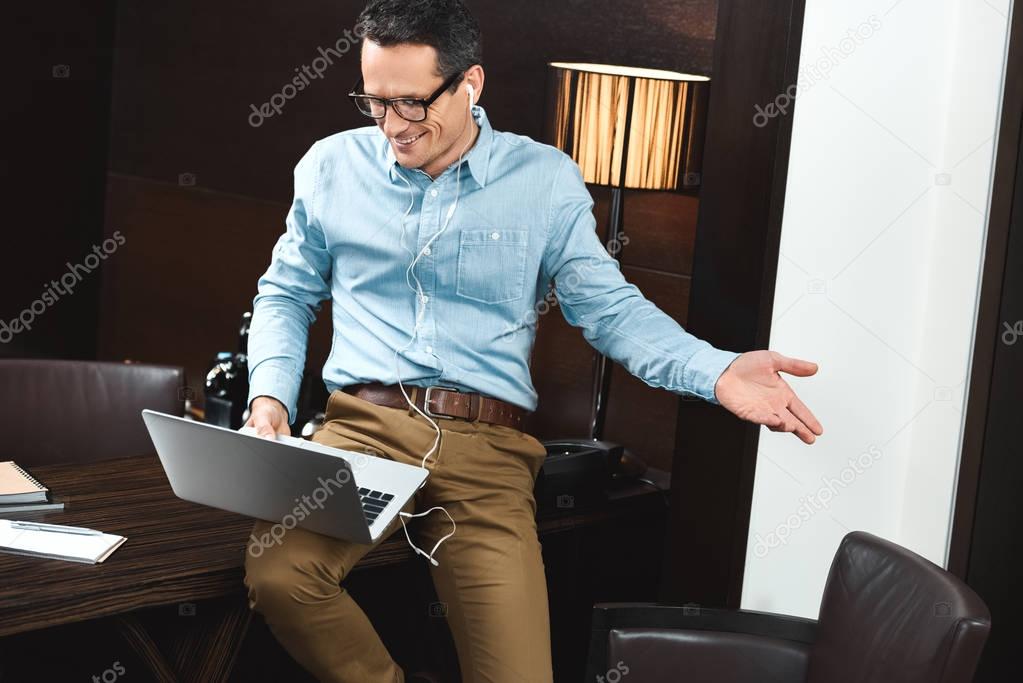 Laughing businessman in headphones using laptop