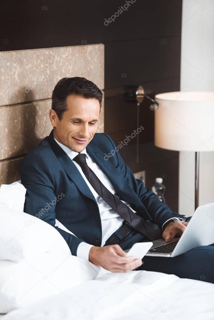 businessman on bed with smartphone and laptop