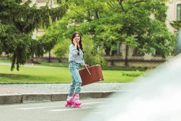 Girl in roller skates with smartphone and suitcase — Free Stock Photo