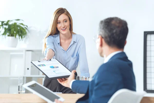 Businesswoman passing clipboard with documents to partner — Stock Photo, Image