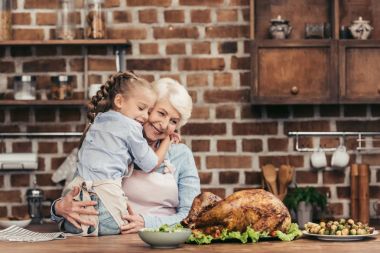 grandmother and granddaughter embracing on kitchen clipart