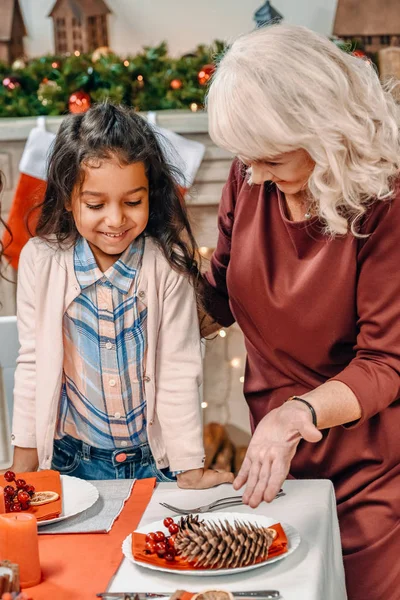 Grandmother decorating christmas table with granddaughter — Stock Photo, Image