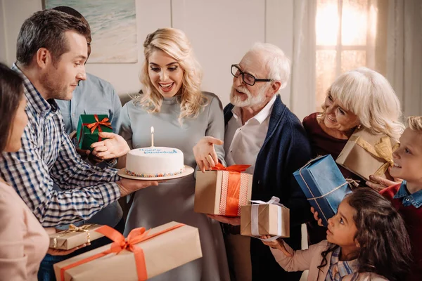 Family presenting cake and gifts to woman — Stock Photo, Image