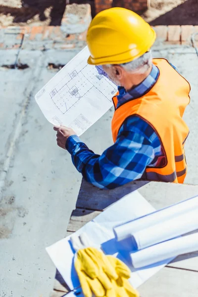 Trabalhador da construção civil que examina planos de construção — Fotografia de Stock