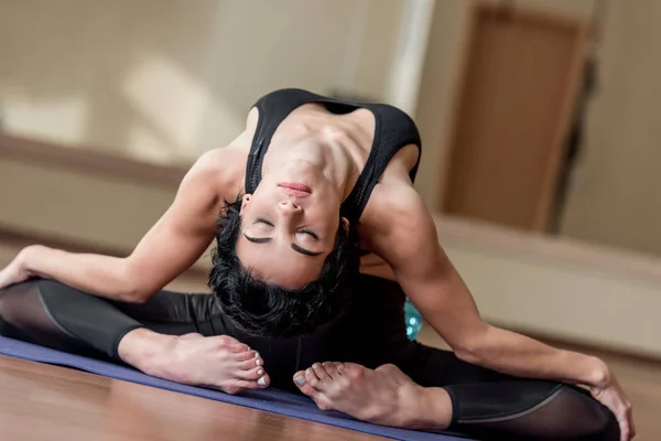 Гибкая женщина сидит на коврике для йоги — стоковое фото