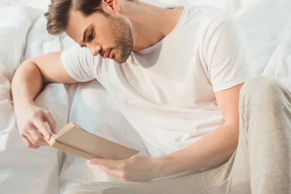 Человек читает книгу в постели — стоковое фото