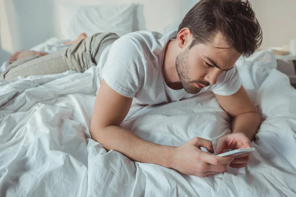Okostelefont használó férfi az ágyban — Stock Fotó