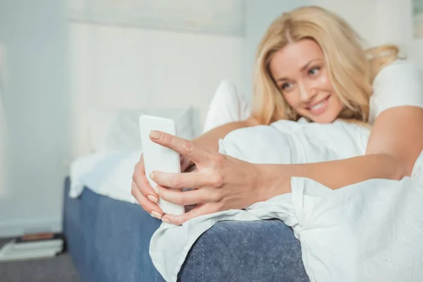 침대에서 스마트폰을 사용하는 여성 — 스톡 사진