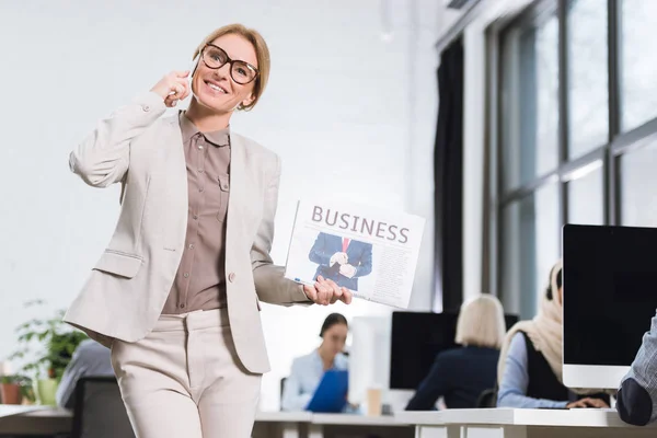 Businesswoman with newspaper talking on smartphone — Stock Photo, Image
