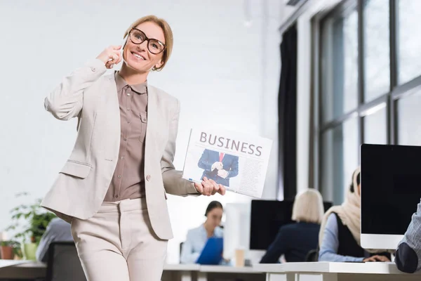 Empresária com jornal falando no smartphone — Fotografia de Stock