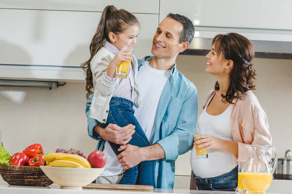 happy family with juice, vegetables and fruits at kitchen looking at each other