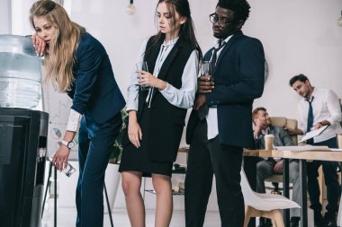 overworked businesspeople standing in queue for water dispenser at office clipart