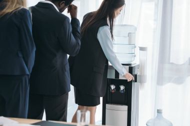 businesspeople standing in queue for water dispenser at office clipart